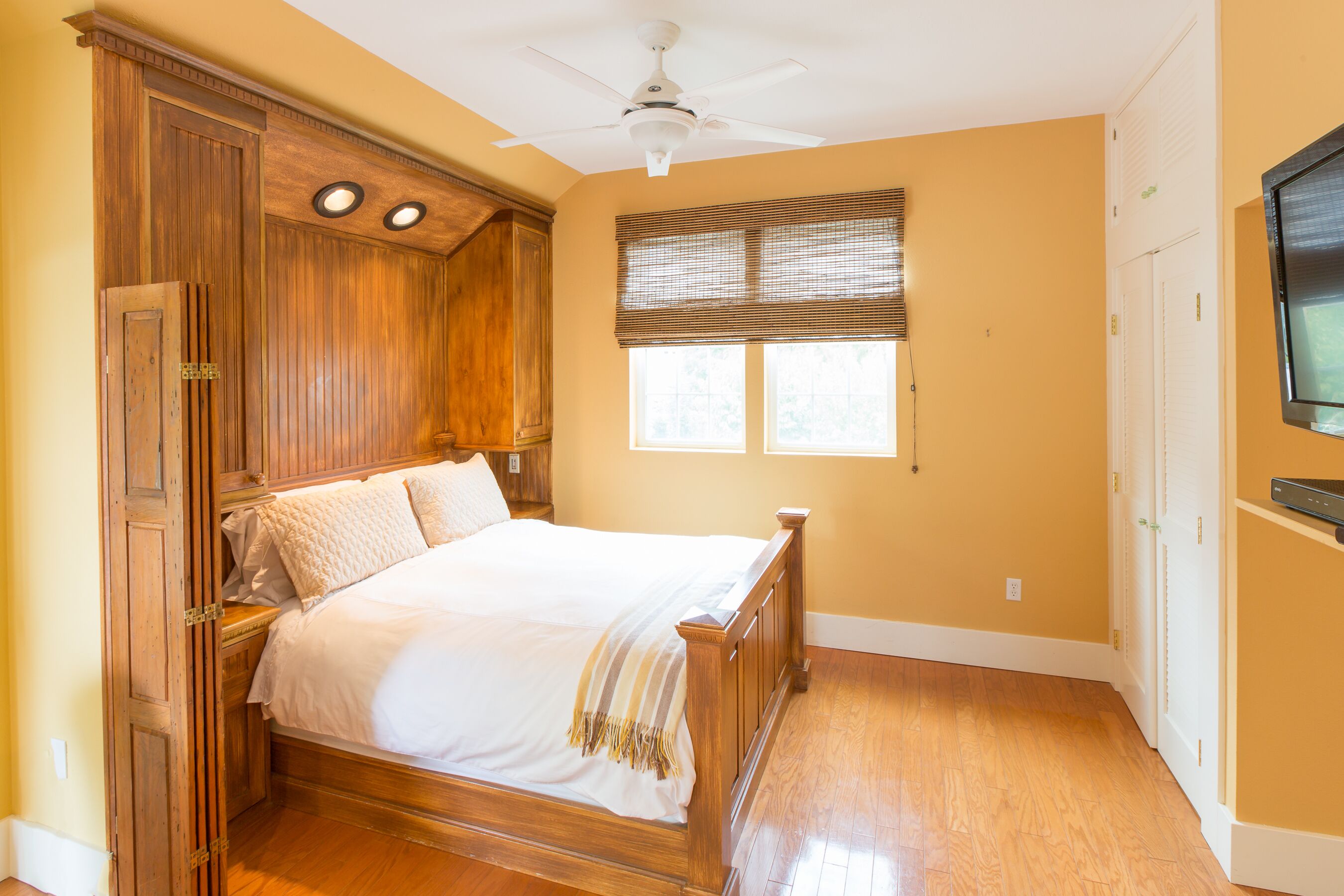 Quarto com cama de madeira, ventoinha no teto e janela com persianas.