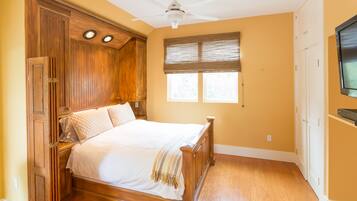 Quarto com cama de madeira, ventoinha no teto e janela com persianas.