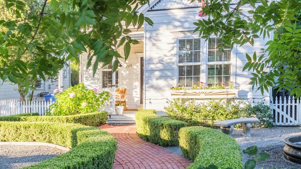 A garden pathway leading to a white building with a traditional design, surrounded by neatly trimmed hedges and a white picket fence. - Inn St Helena (St. Helena)