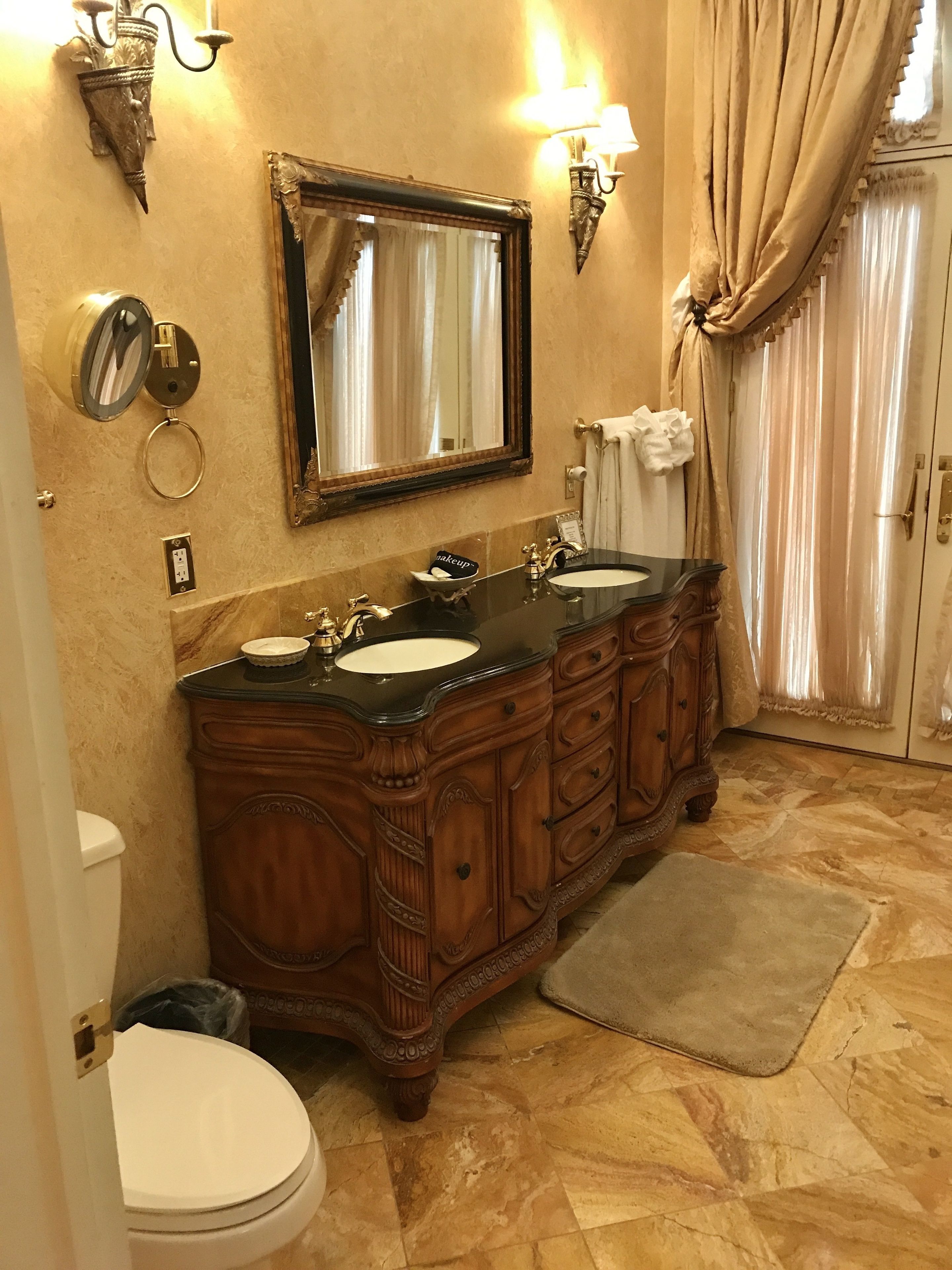 Une salle de bain avec un meuble-lavabo à deux vasques, un grand miroir, des appliques murales et des toilettes.