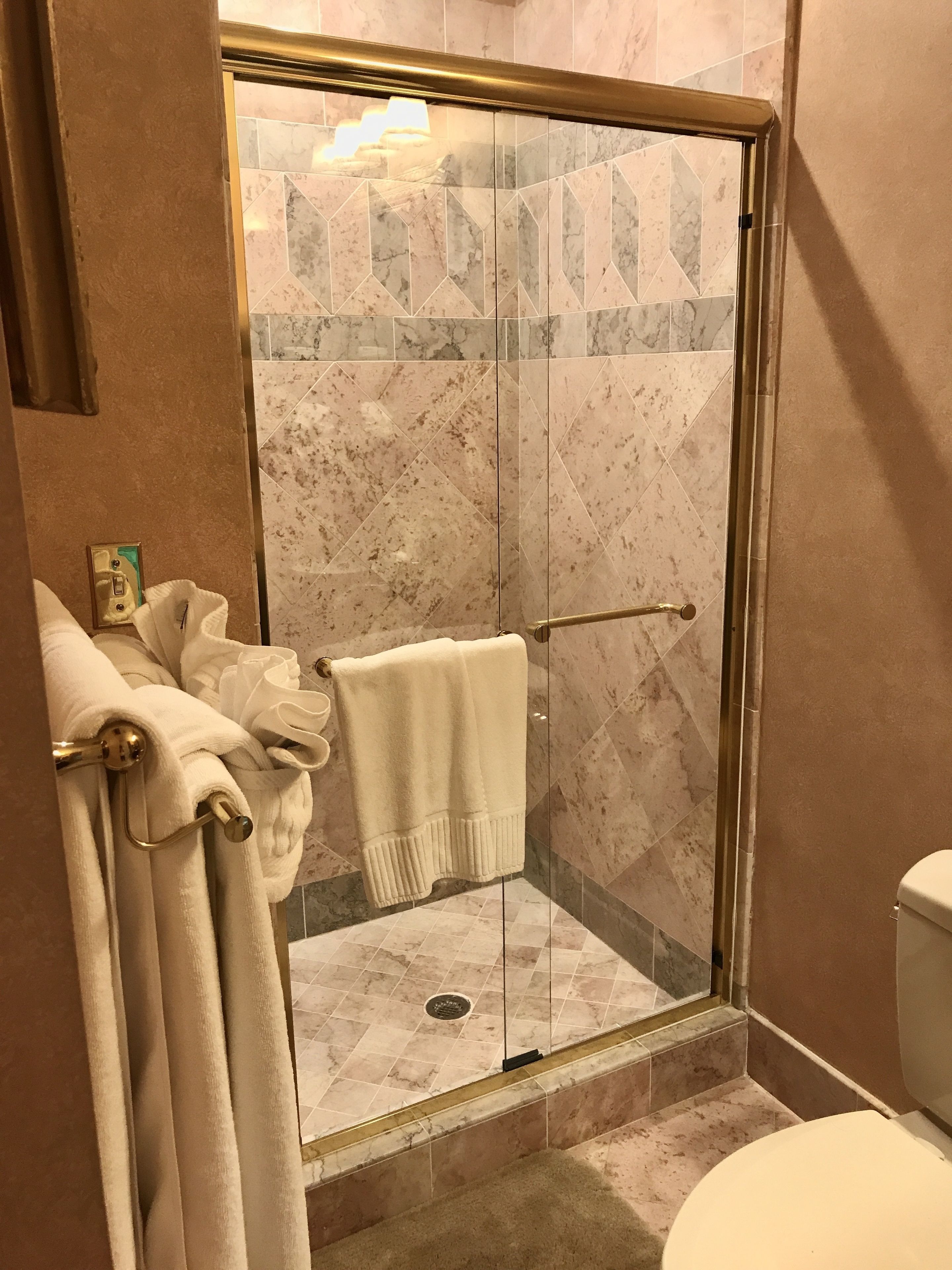 A glass-enclosed shower with a marble-tiled floor, a towel rack with towels, and a toilet.