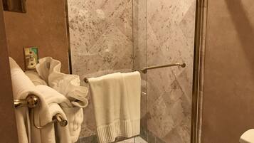 A glass-enclosed shower with a marble-tiled floor, a towel rack with towels, and a toilet.