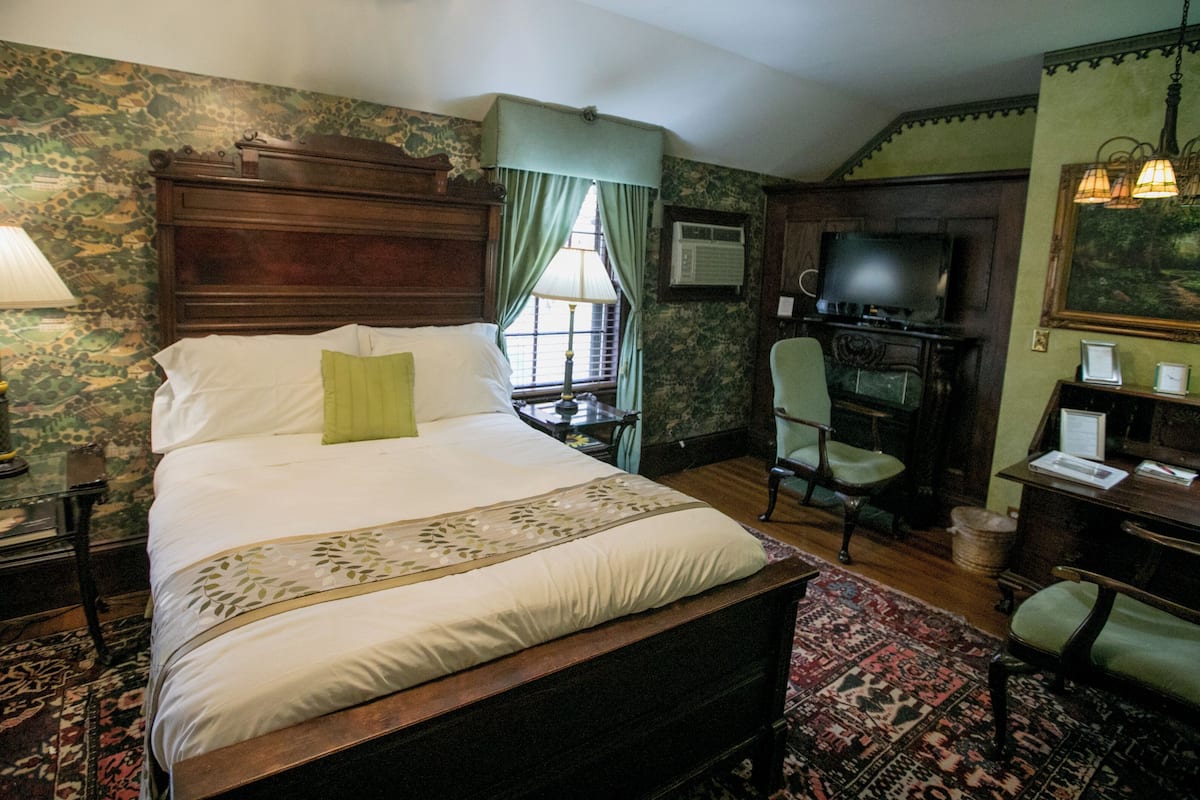 A bedroom with a large bed, a desk with a chair, a television, and a window with curtains.