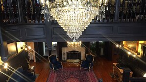 A grand room with a large chandelier, two blue armchairs, a red patterned rug, and a fireplace.