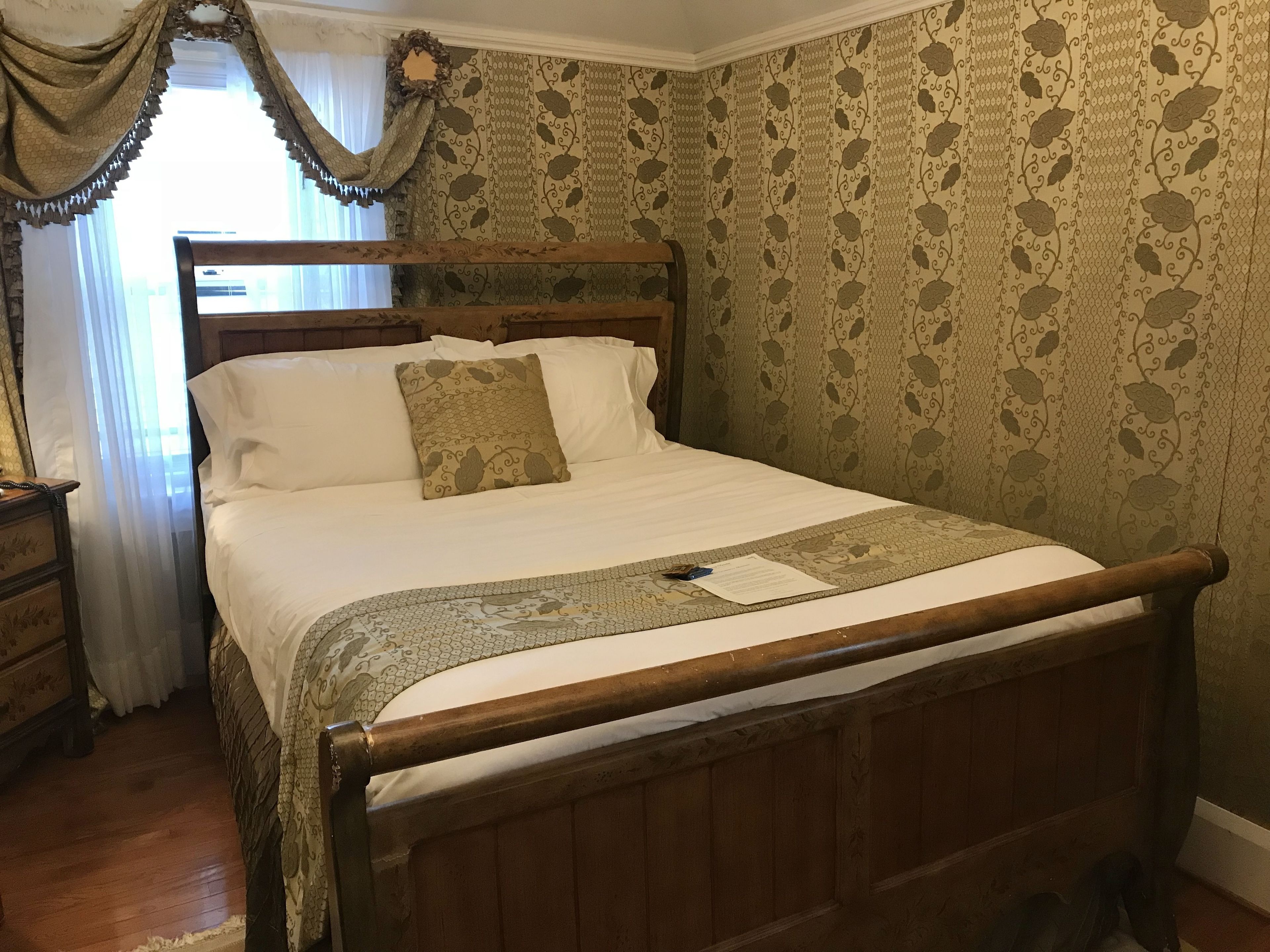 Una cama de madera con cabecera, ropa de cama blanca y una colcha estampada.