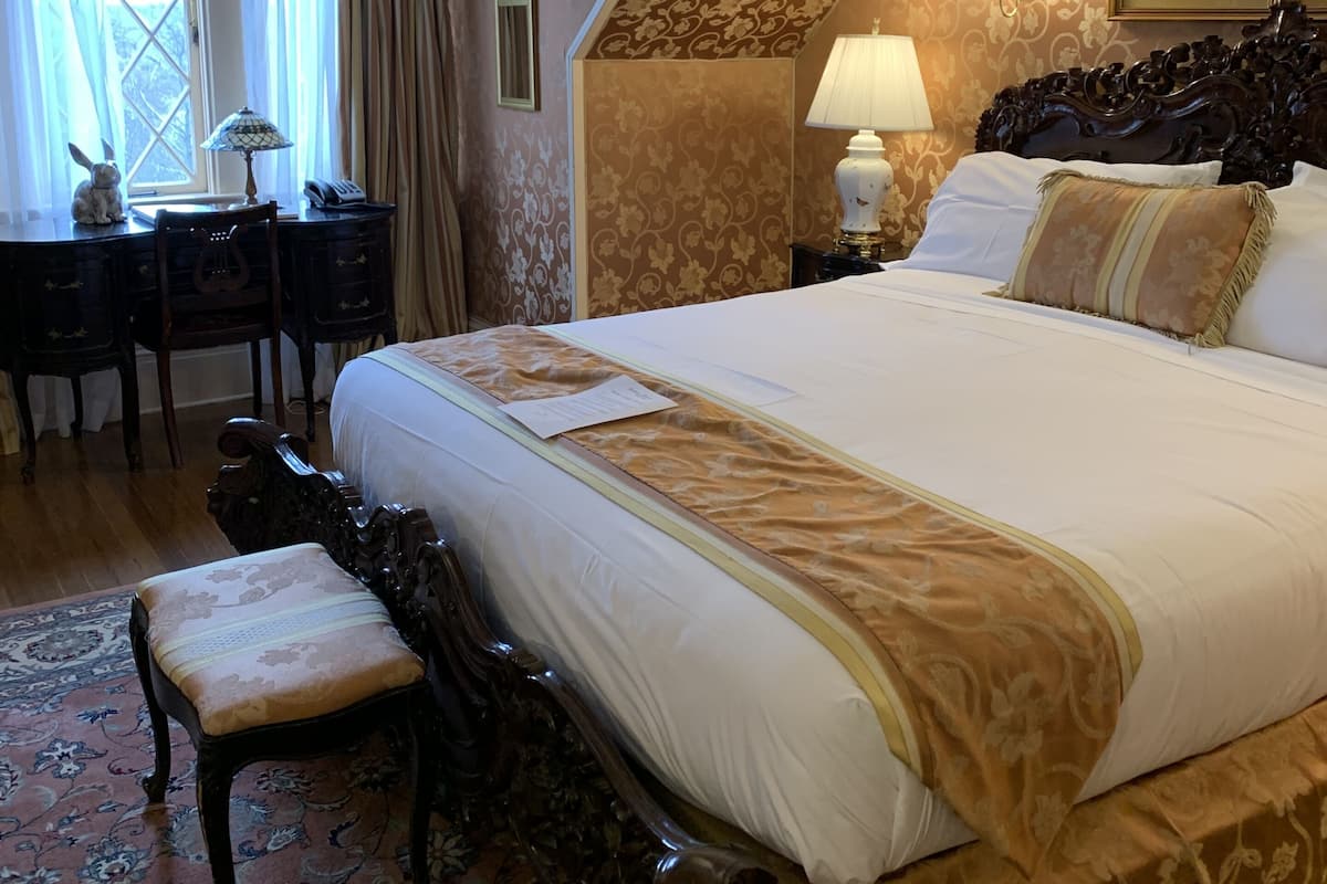 A hotel room with a large bed, a desk with a lamp, a chair, and a window with curtains.