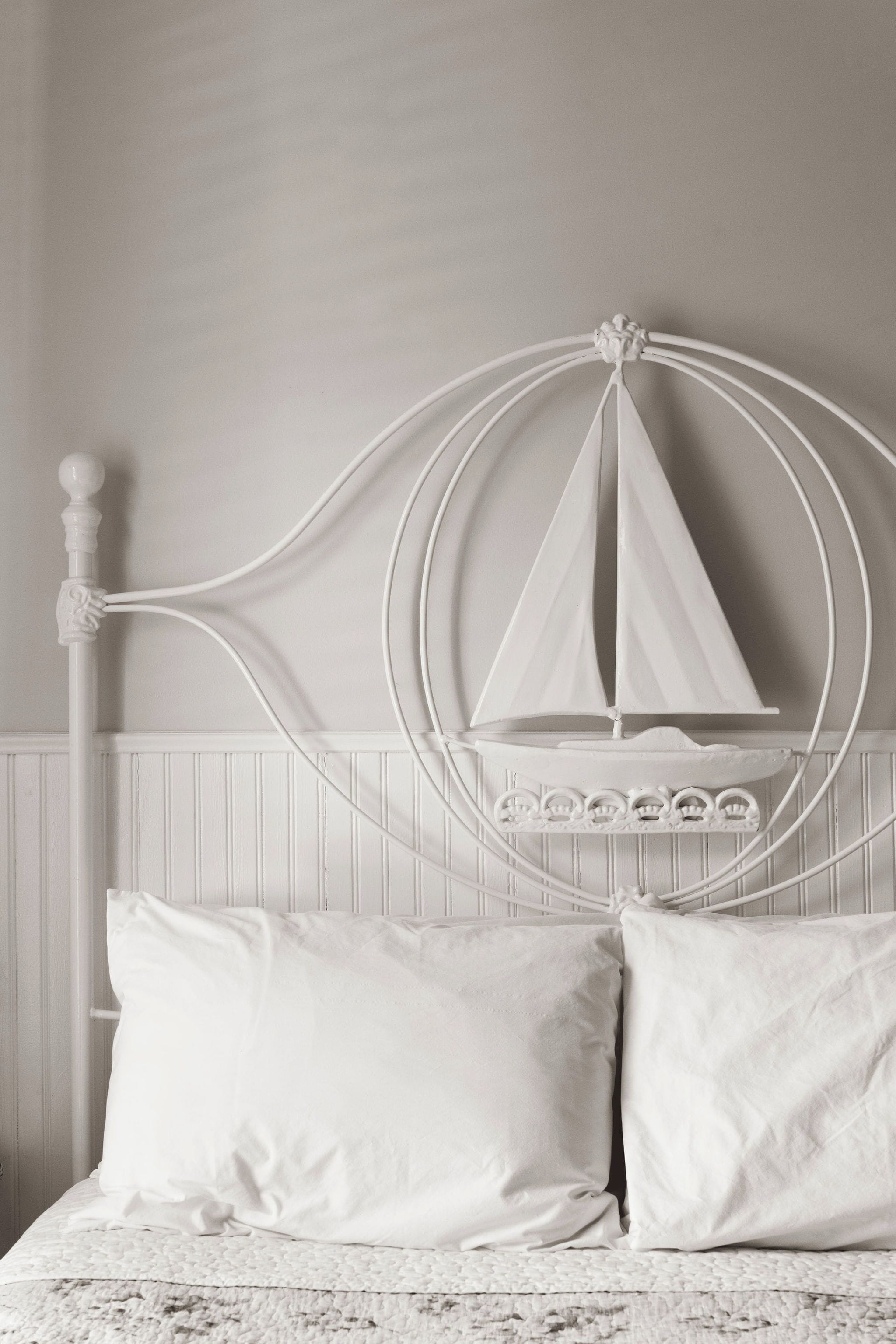 A bed with a white headboard featuring a sailboat design, two pillows, and a textured blanket.