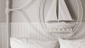 Una cama con cabecera blanca decorada con un diseño de velero, dos almohadas y una manta con textura.