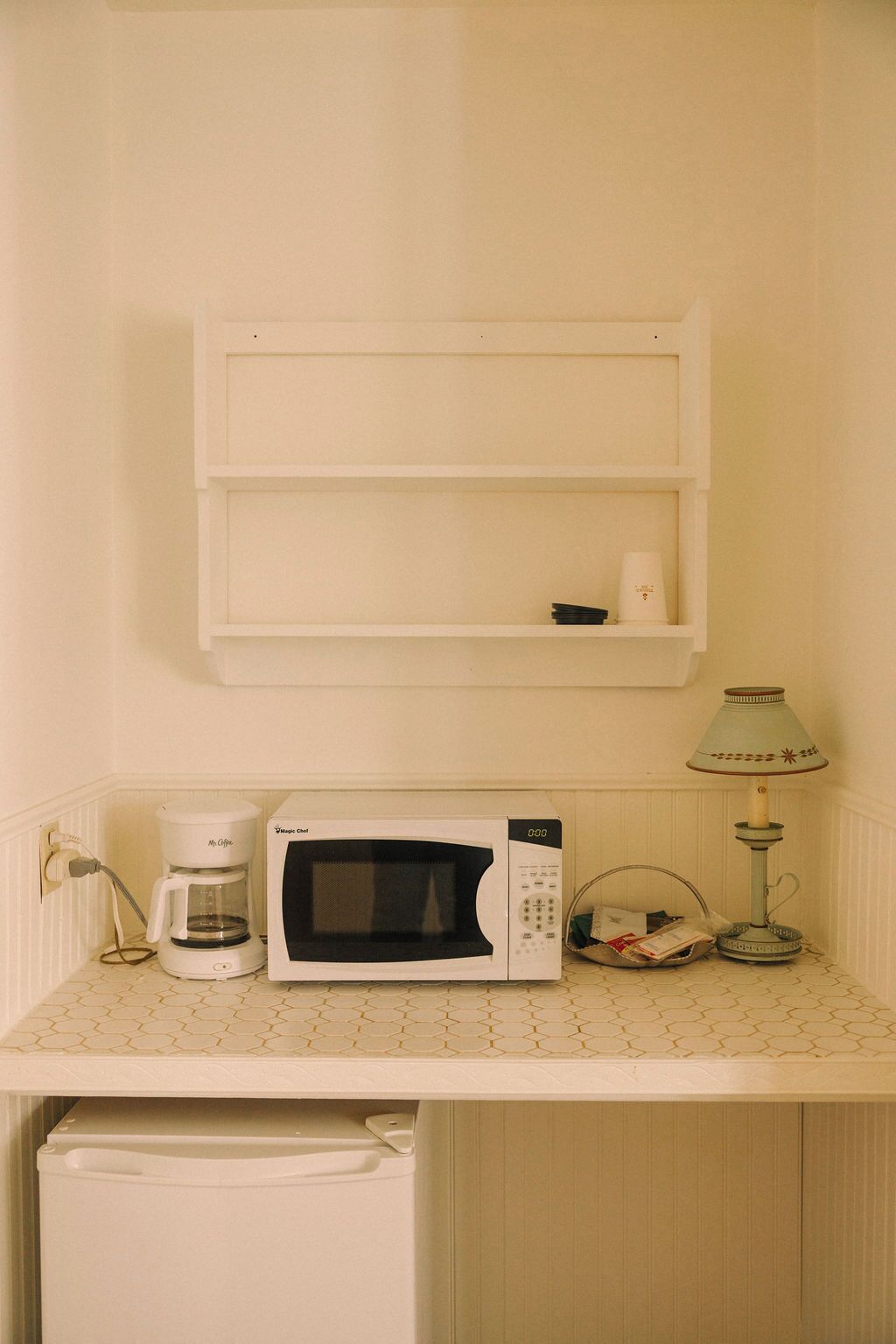 Een kitchenette met een magnetron, koffiezetapparaat en een lamp op een aanrecht met een honingraatpatroon.