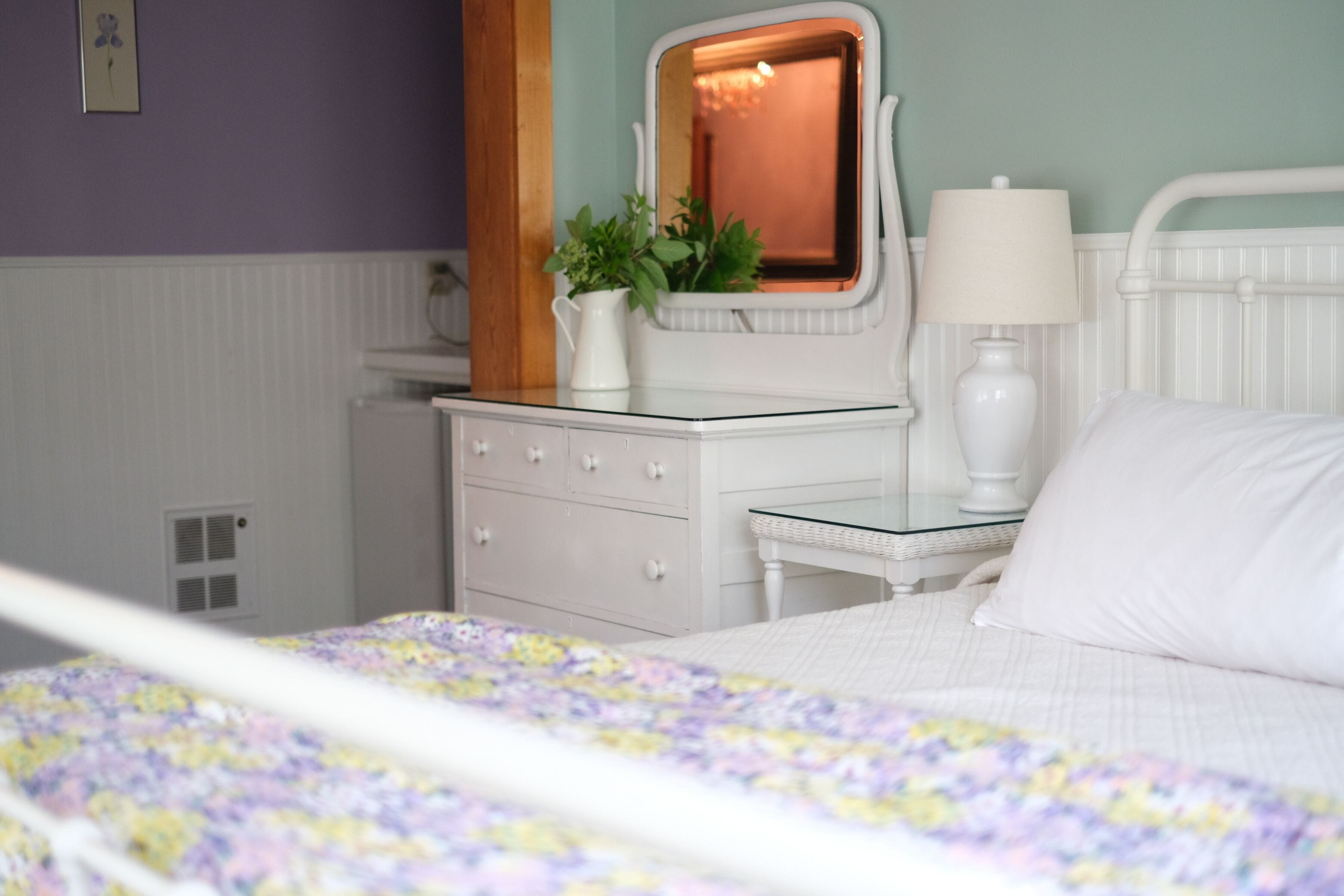 A bedroom with a bed, dresser, mirror, lamp, and a potted plant.
