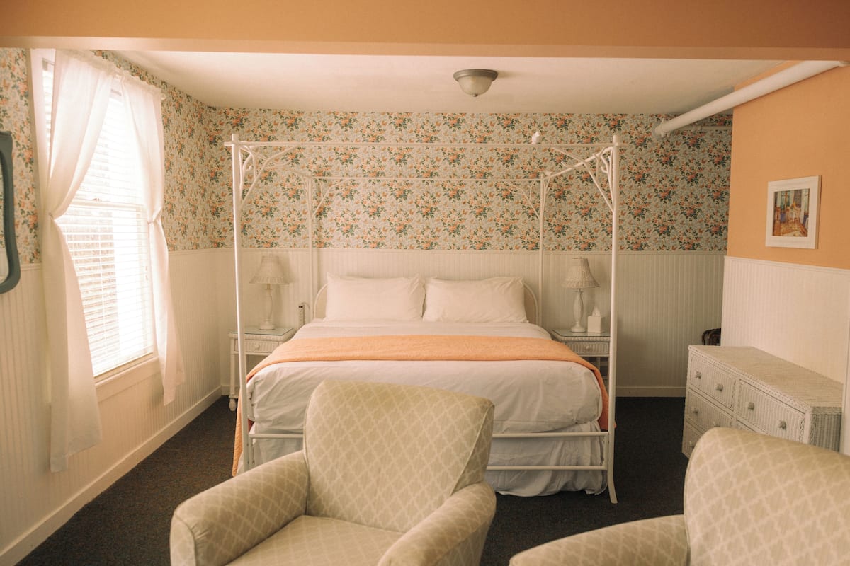 A bedroom with a four-poster bed, two bedside tables, a nightstand, a chair, and a dresser.