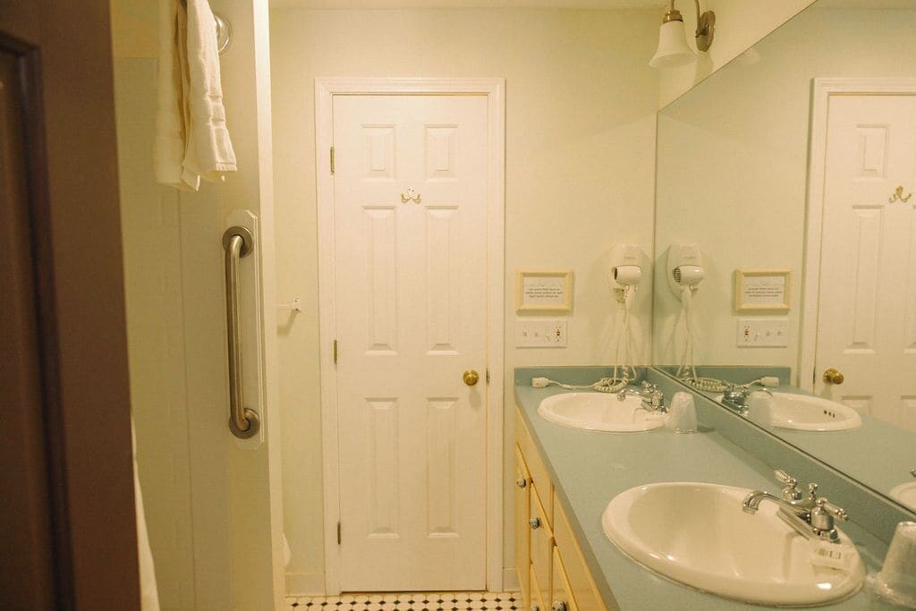 A bathroom with two sinks, a large mirror, and a door with a handrail.