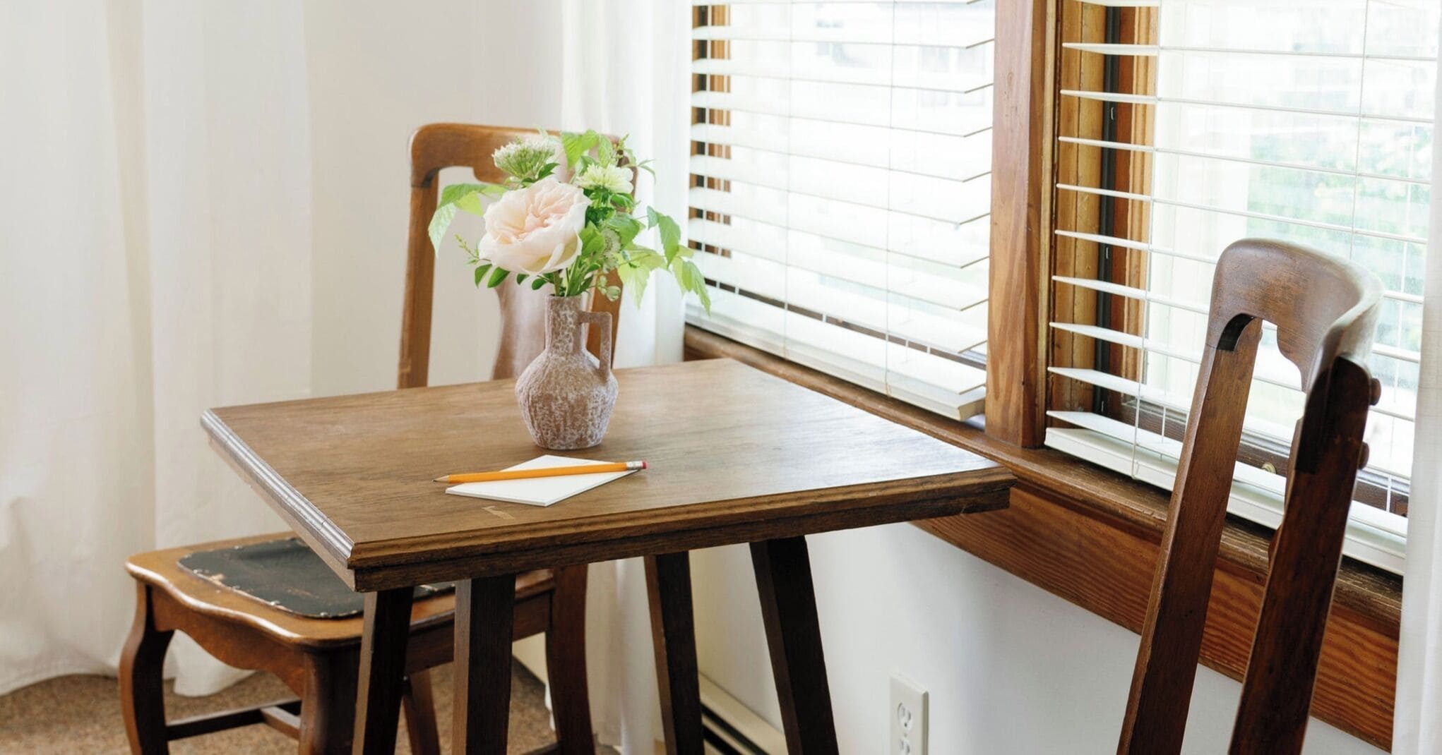 Una mesa de madera para comer con un florero y un bloc de notas.