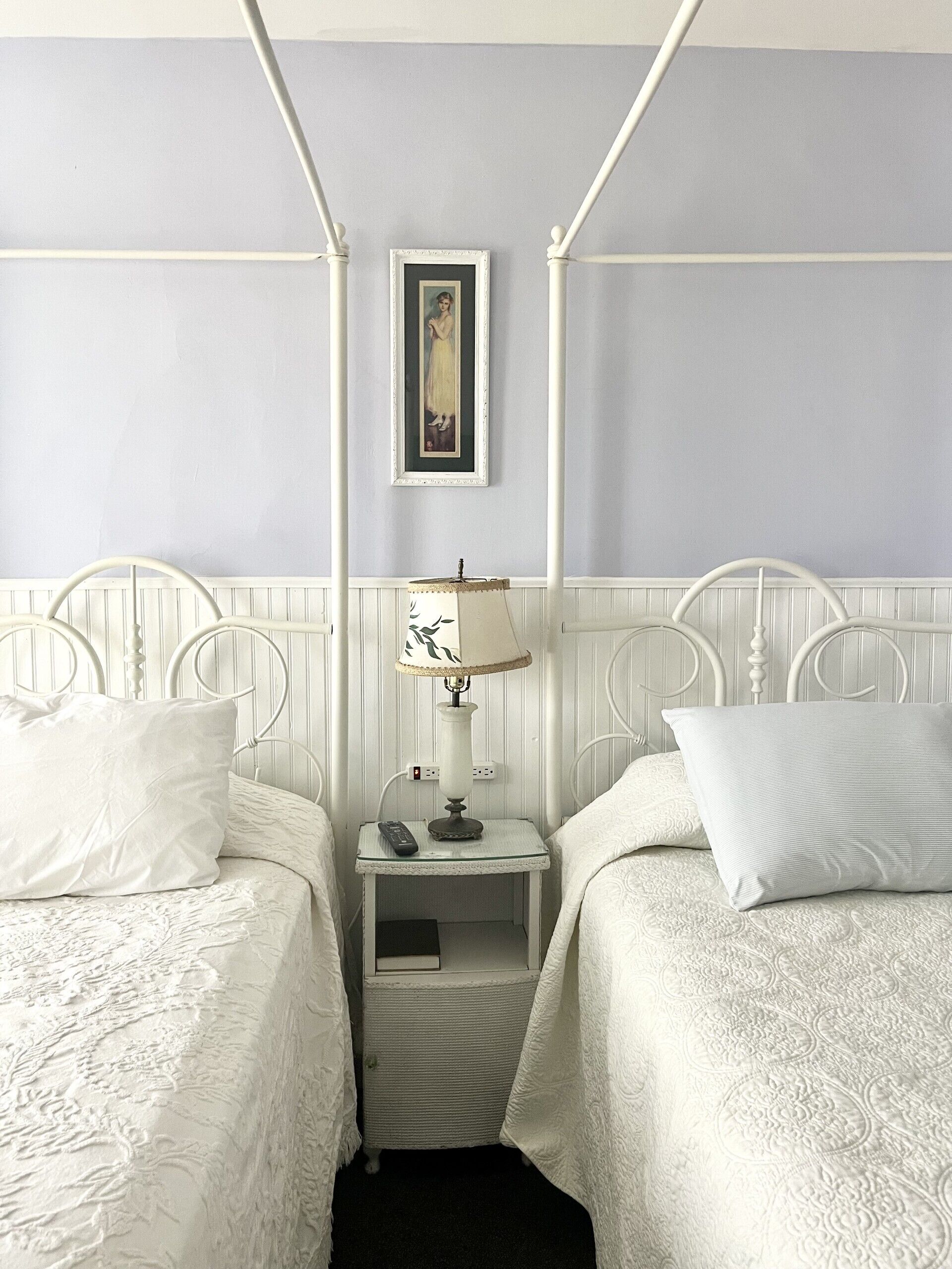A four-poster bed with white bedding and a small bedside table with a lamp.