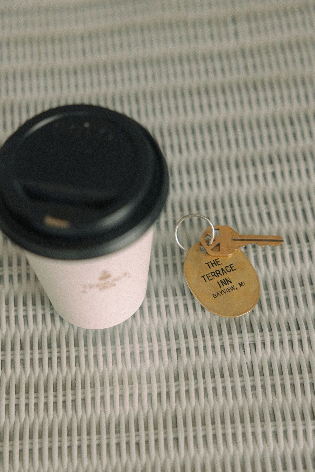 A coffee cup with a black lid and a keychain with a tag that reads "The Terrace Inn Bayview, MI".