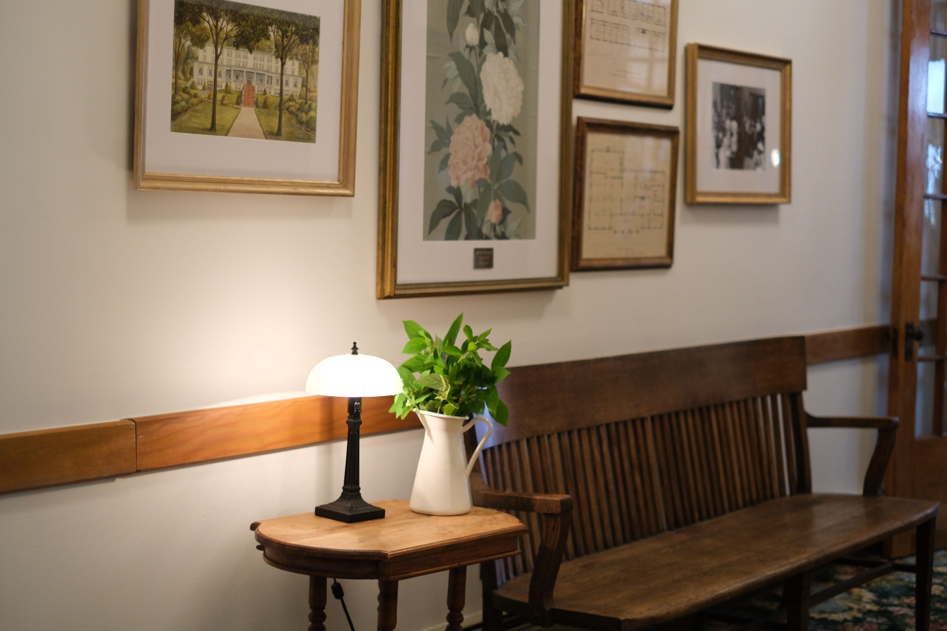 Een bank, een tafel met een lamp en een vaas met een plant, en ingekaderde foto's aan de muur.