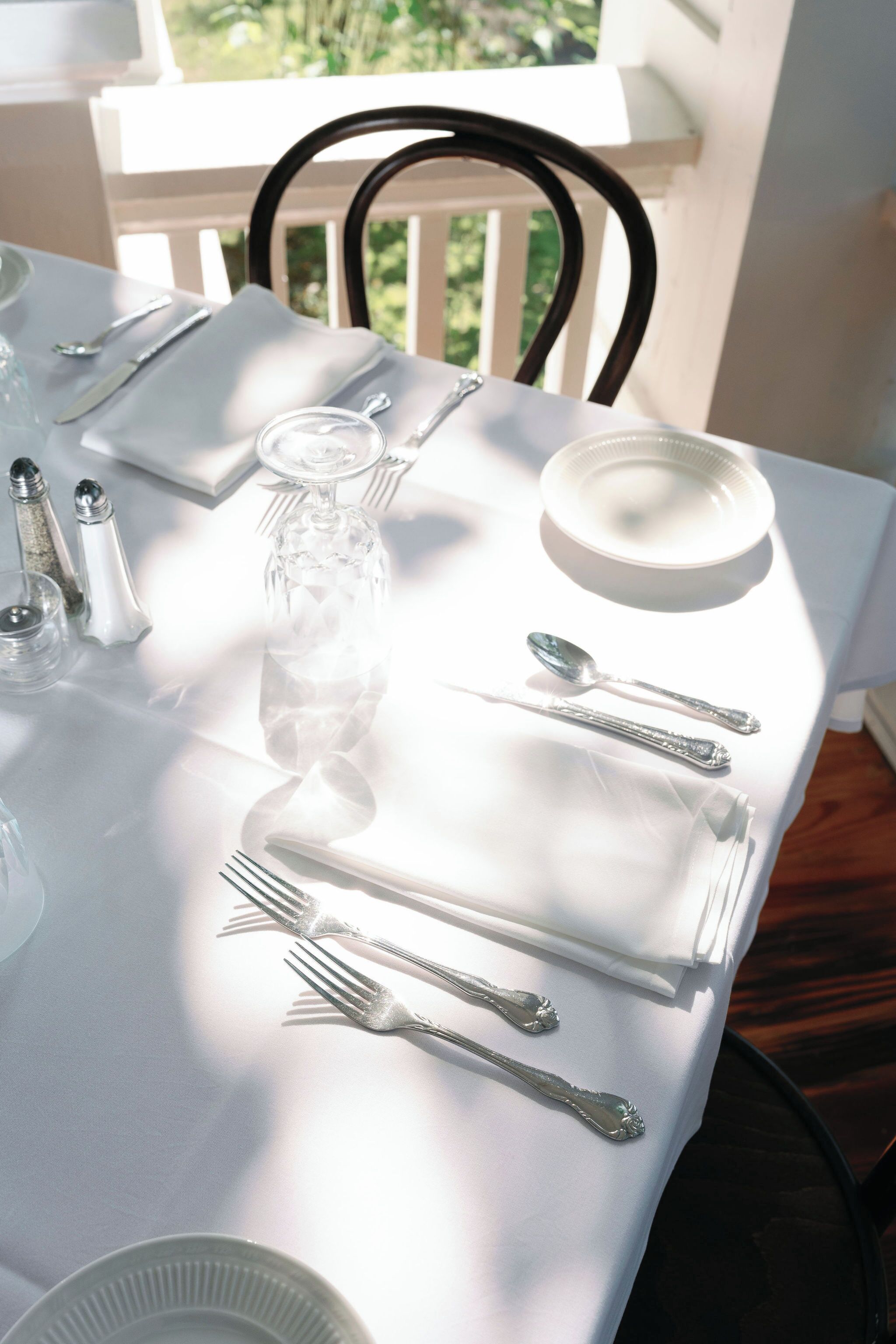 Una mesa dispuesta con mantel blanco, cubiertos y cristalería, con una vista despejada al exterior.
