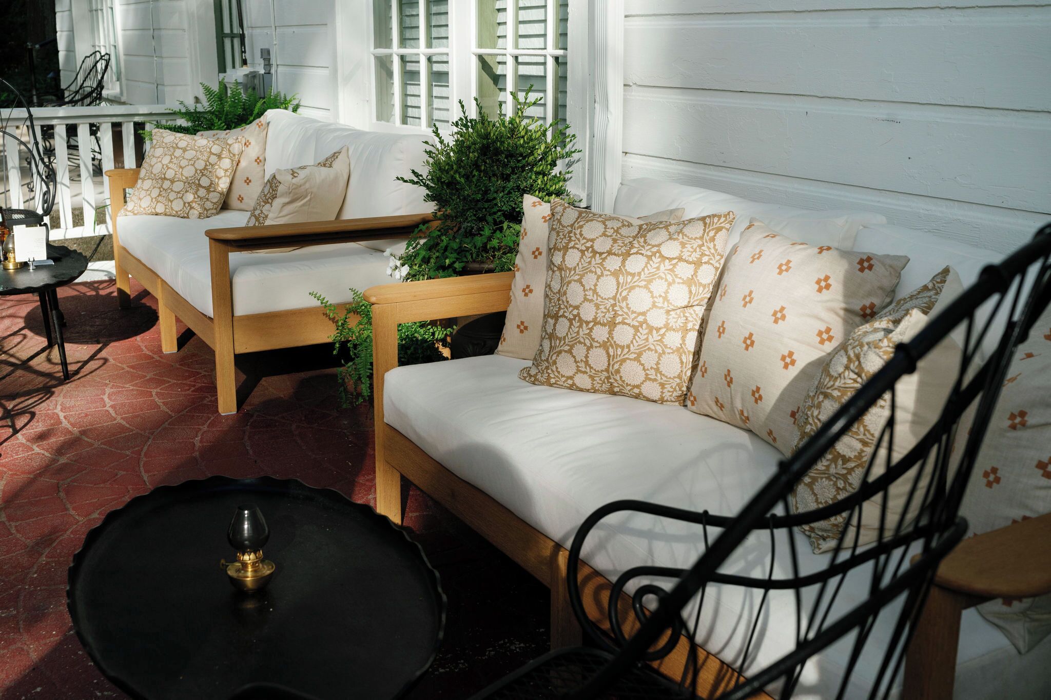 A cozy outdoor seating area with a wooden bench and a sofa, both adorned with patterned cushions.