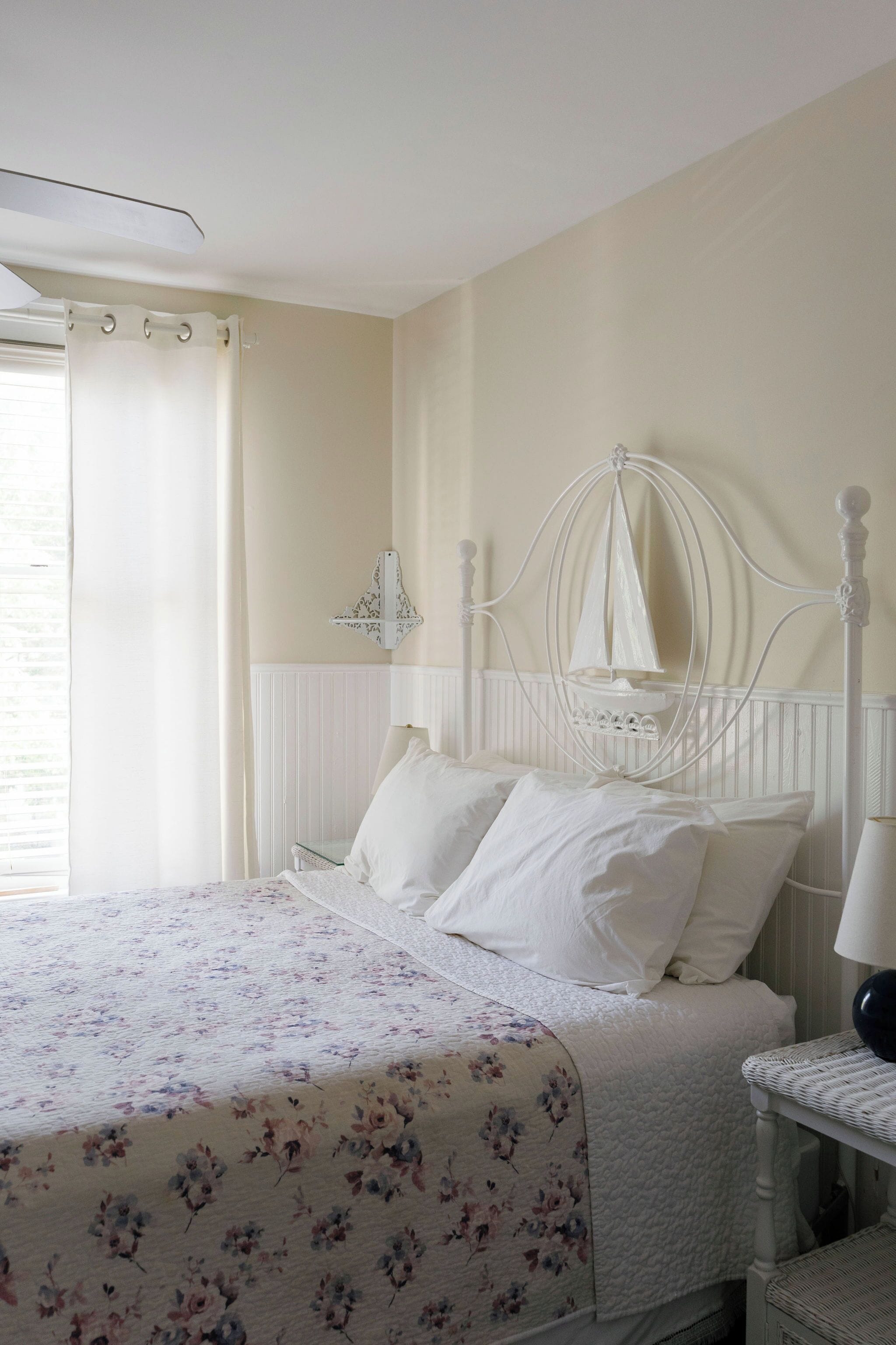 Une chambre à coucher comprenant un lit, une table de chevet, une lampe, une fenêtre avec des rideaux et un luminaire fixé au mur.