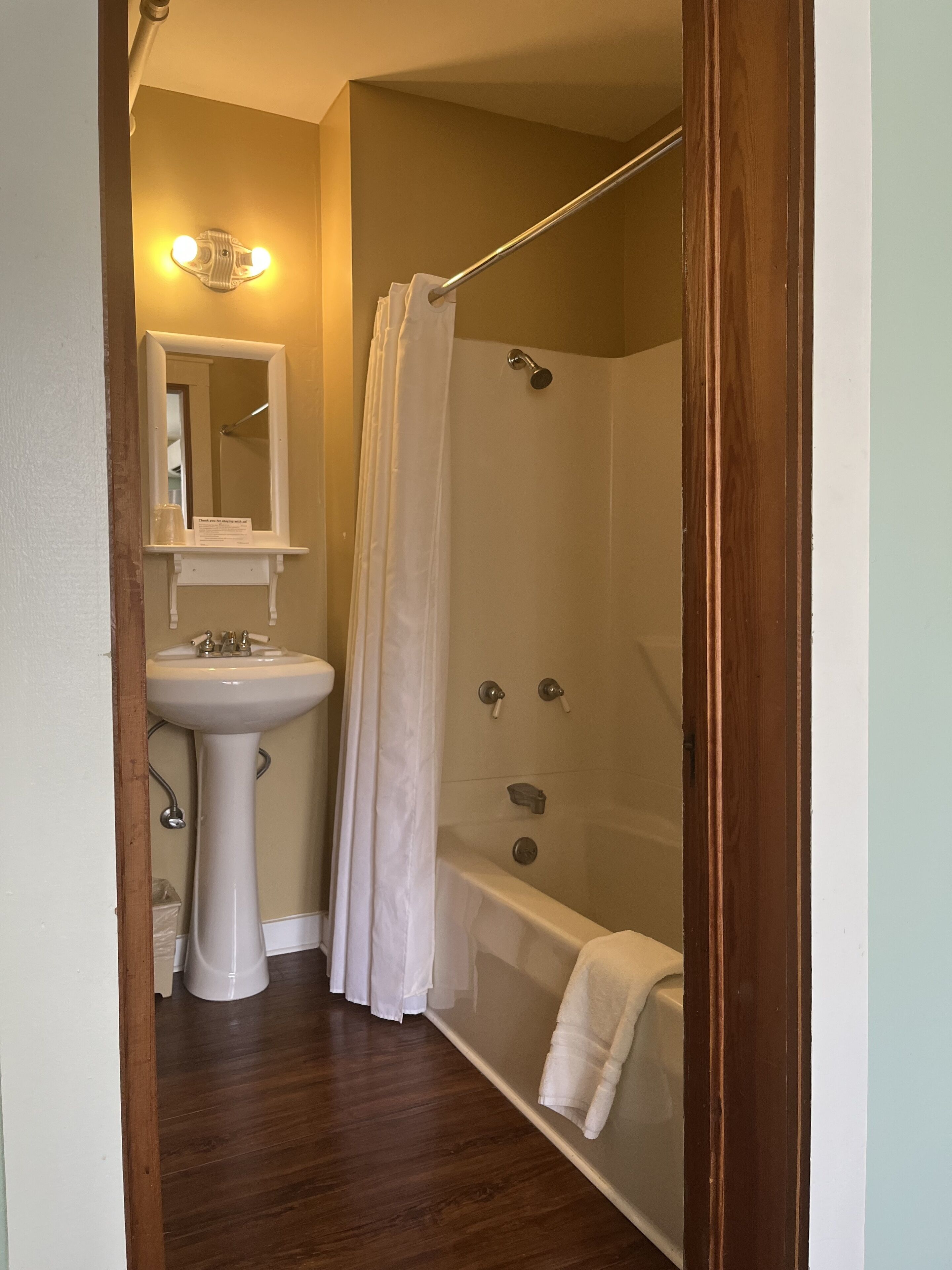 Un baño con lavamanos pedestal, espejo, ducha con puerta de vidrio y bañera.