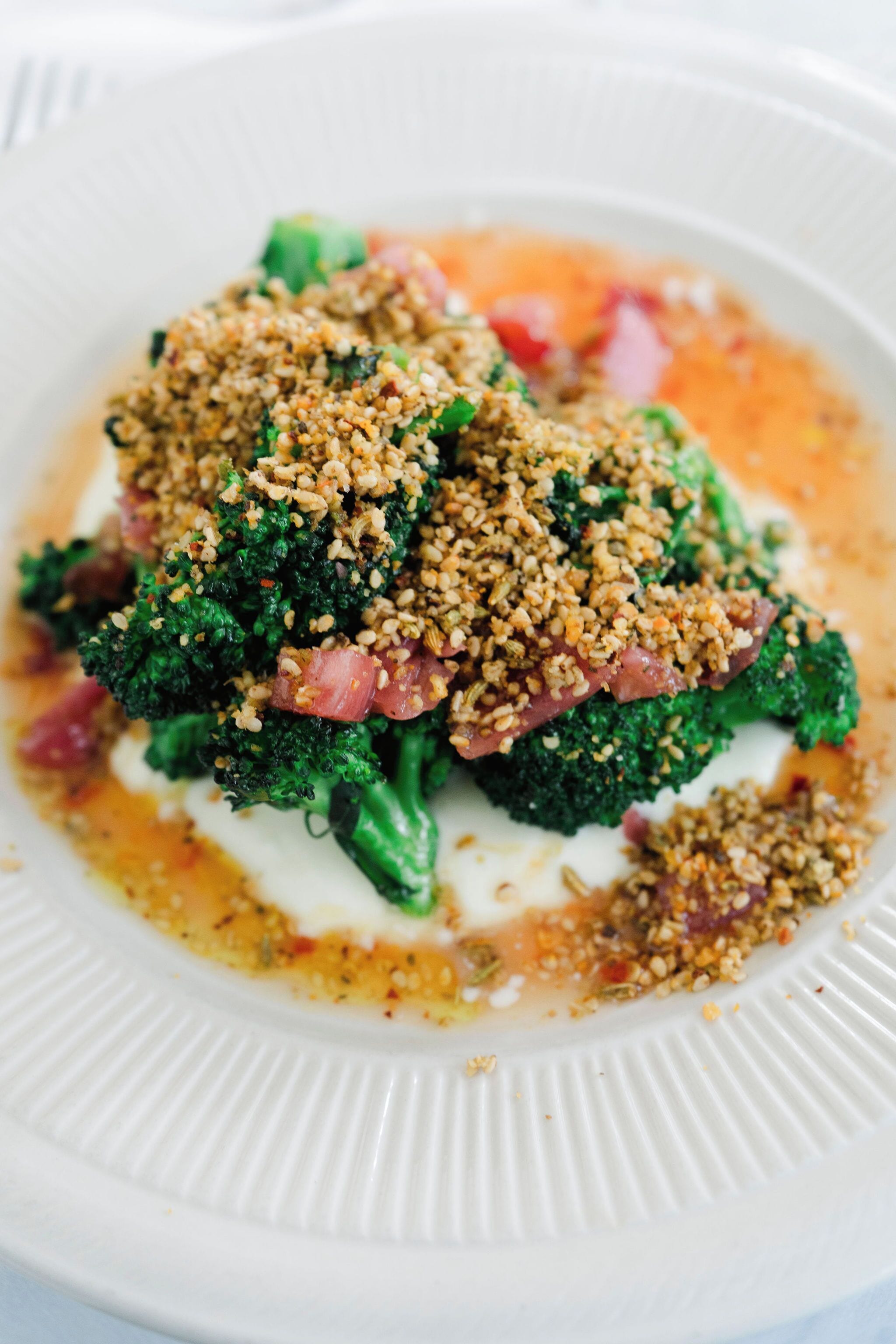 A plate with broccoli topped with a crumbly topping and a creamy sauce.