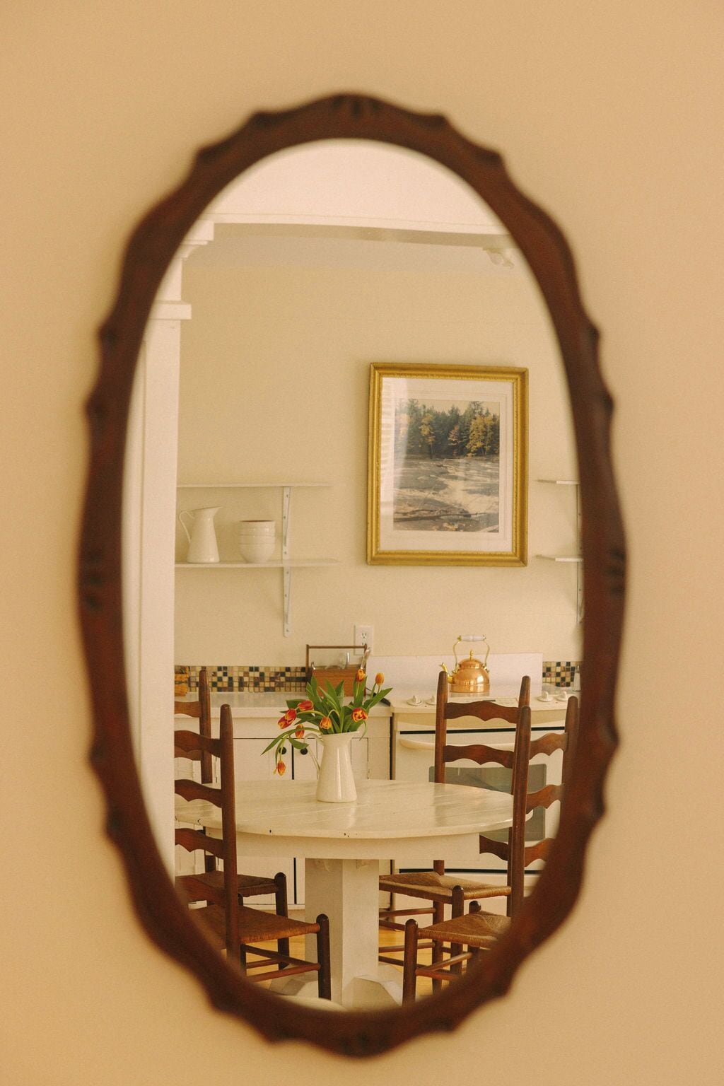Uma sala de jantar com mesa redonda, cadeiras, um vaso com flores e um quadro na parede.