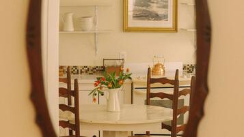 Uma sala de jantar com mesa redonda, cadeiras, um vaso com flores e um quadro na parede.