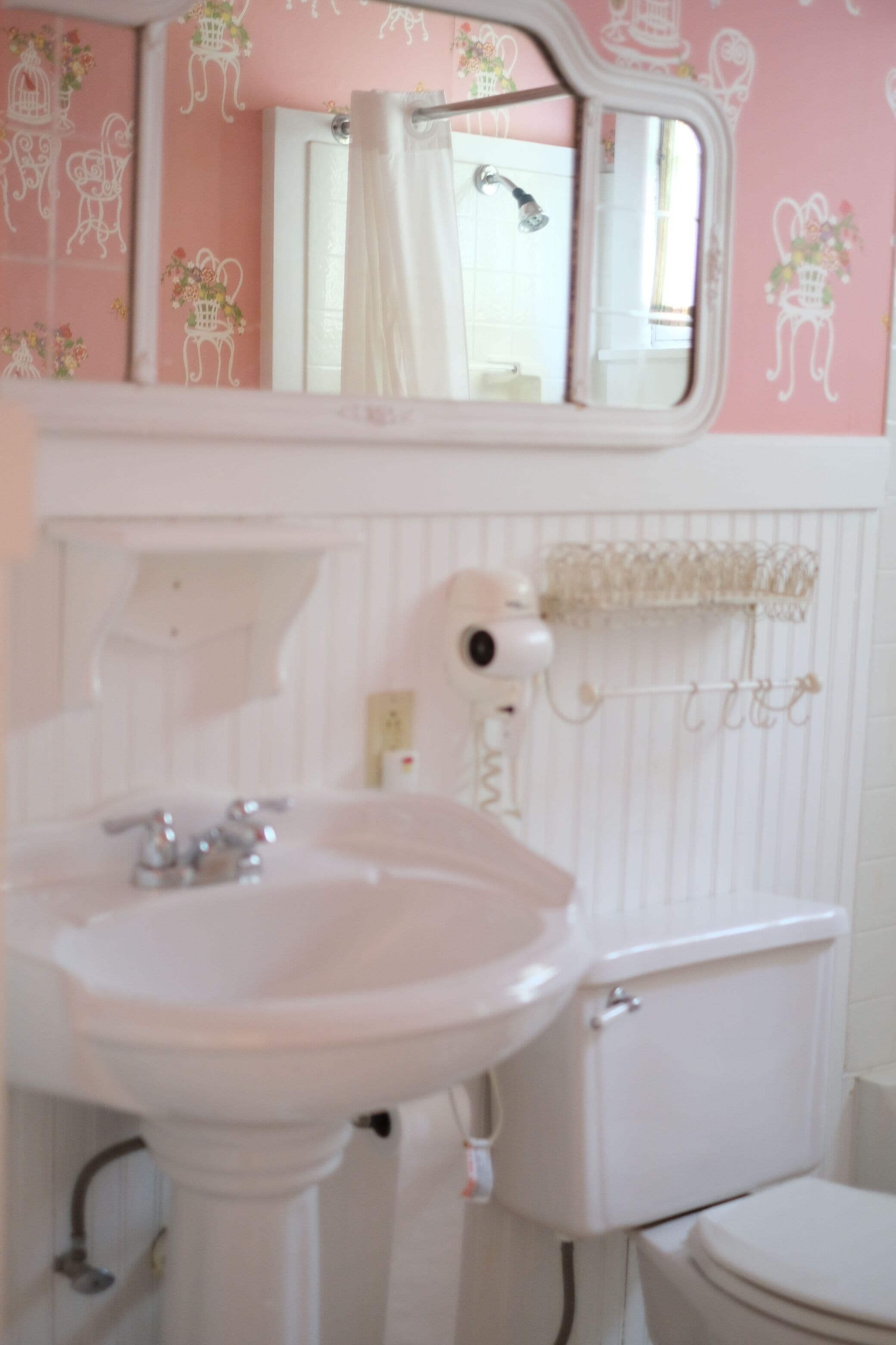 A bathroom with a white sink, mirror, and toilet. The walls have a floral pattern.