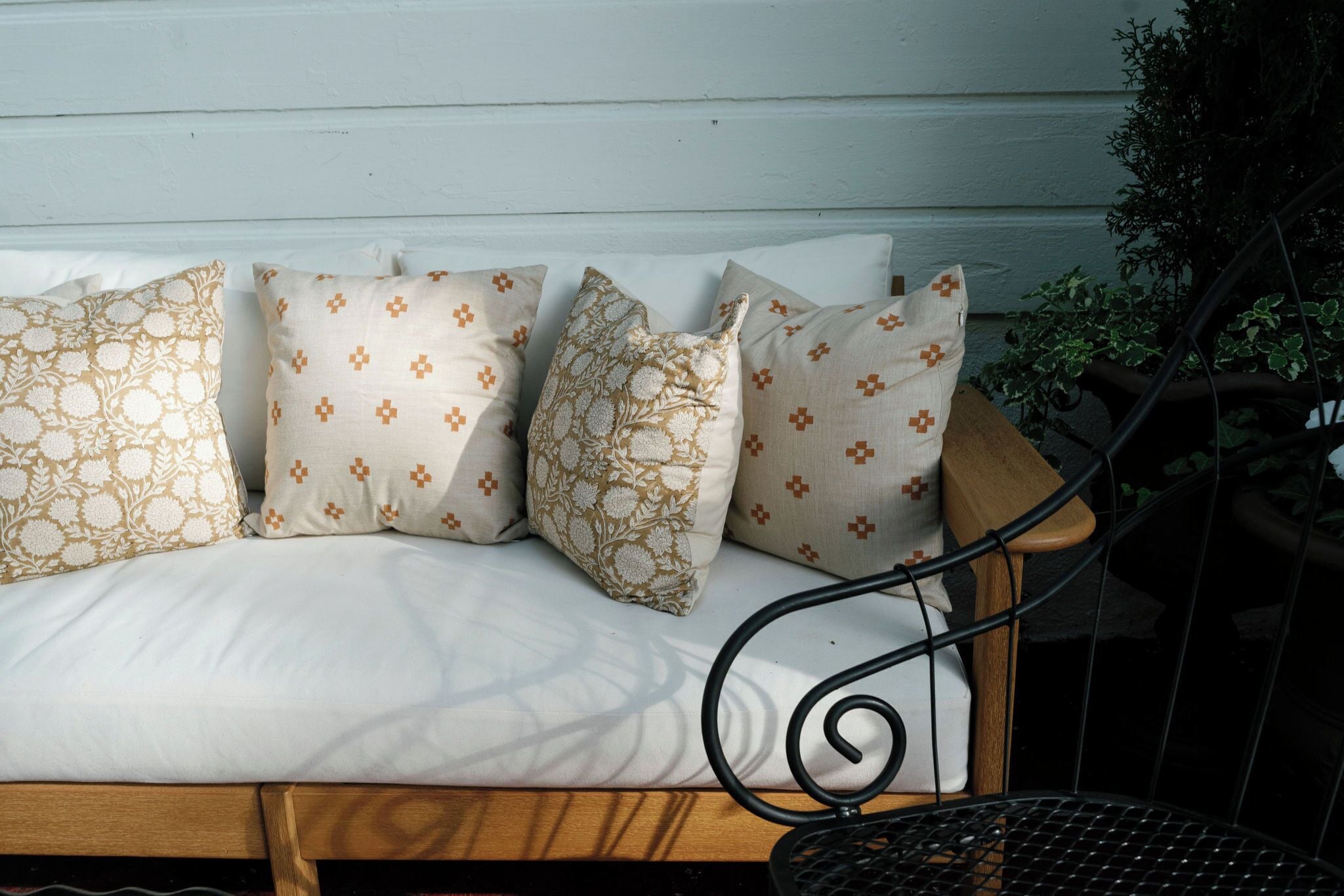 Un banc en bois orné d’un motif en spirale métallique, placé à côté d’un banc blanc avec coussins moelleux aux motifs variés.