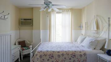 A bedroom with a bed, a chair, a nightstand, a ceiling fan, and a window with curtains.