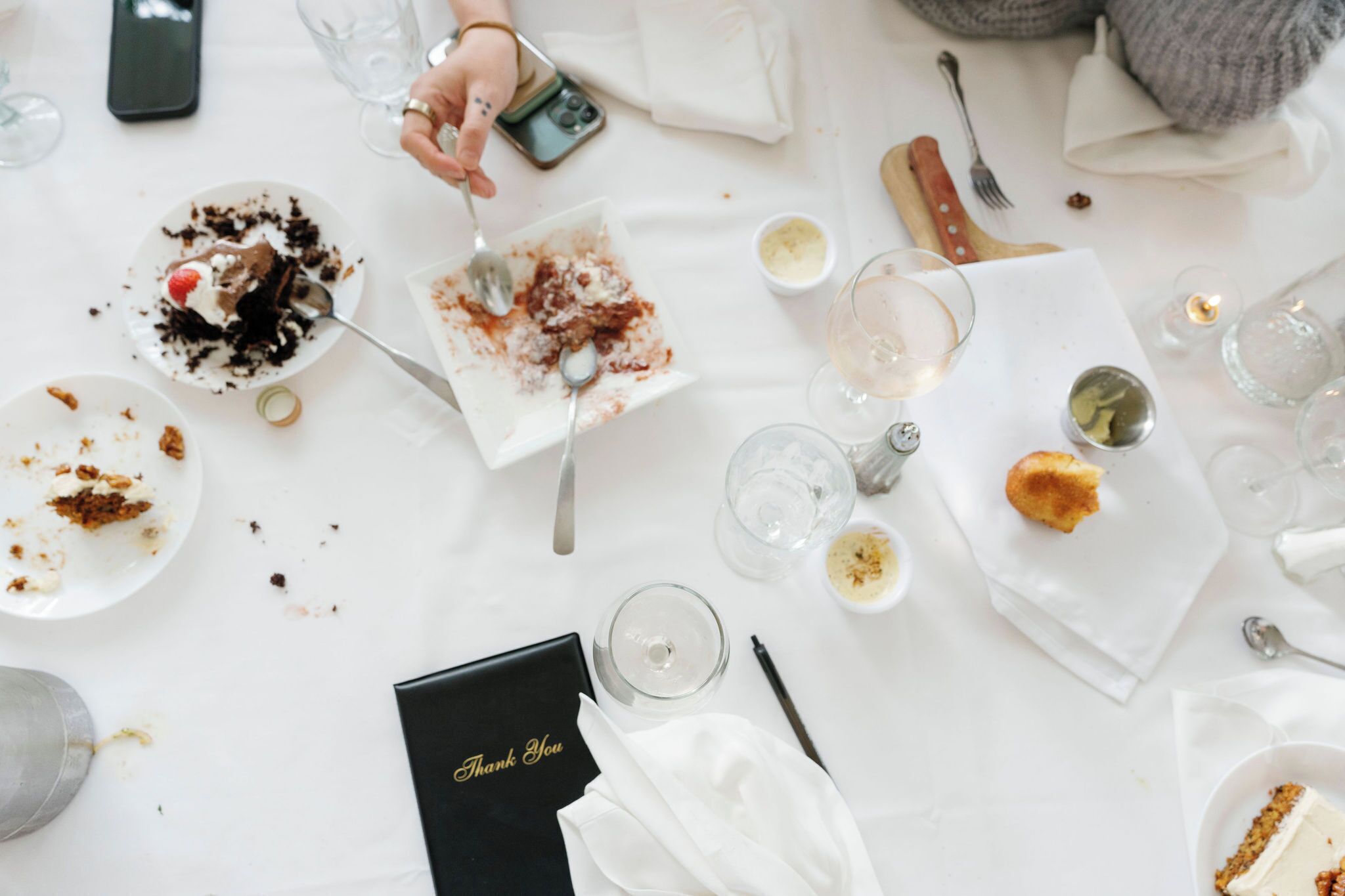 Une table à manger avec des restes de nourriture, des verres à vin et un téléphone intelligent.