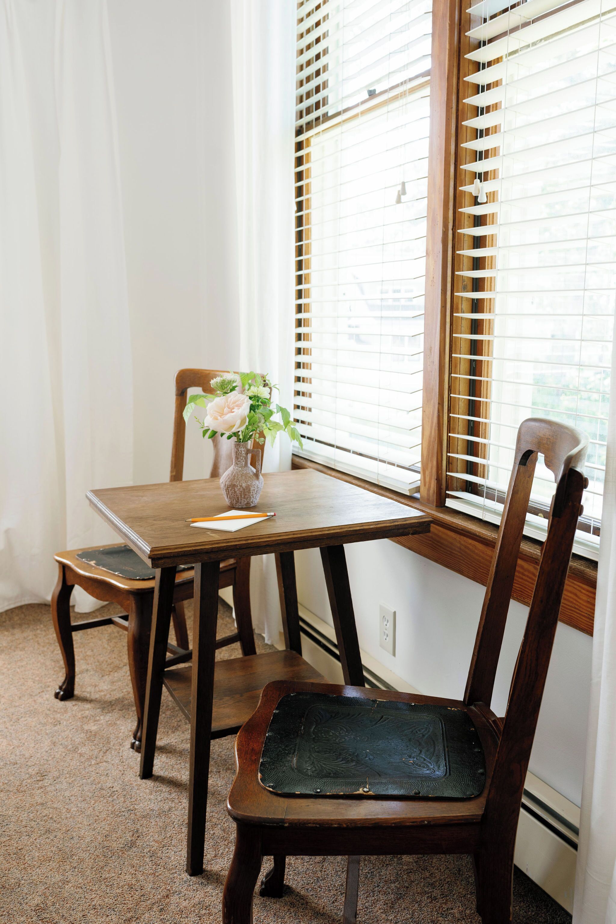 A wooden dining table with a vase of flowers, a chair, and a window with blinds.