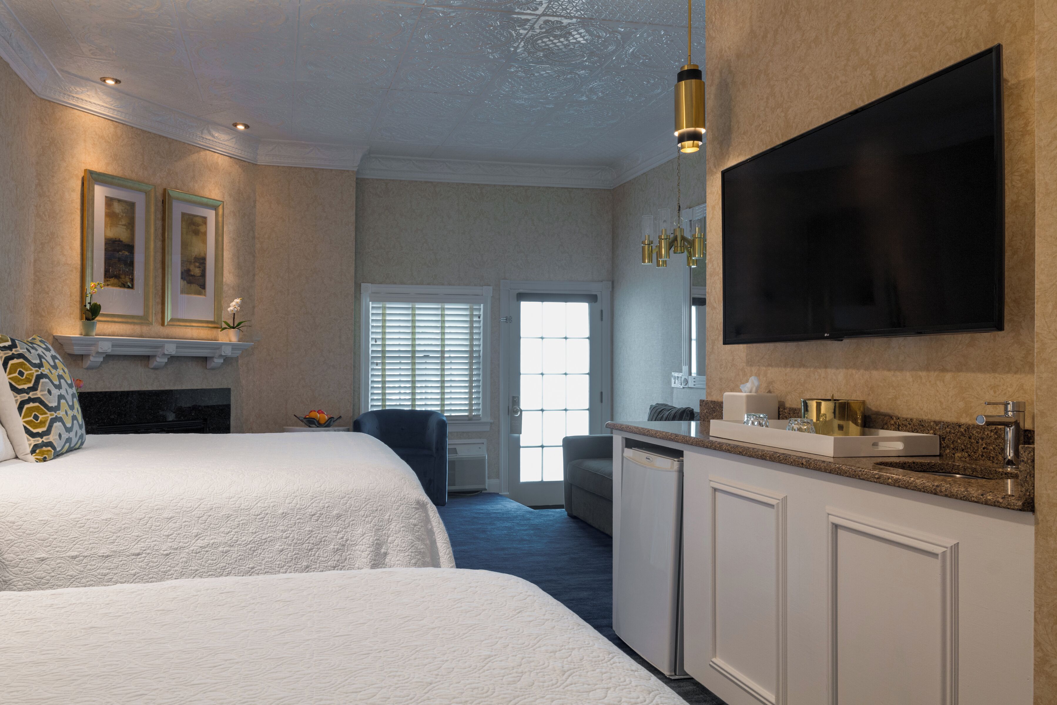 Habitación de hotel con una cama grande, televisor, escritorio con lavamanos y puerta que da a un balcón.