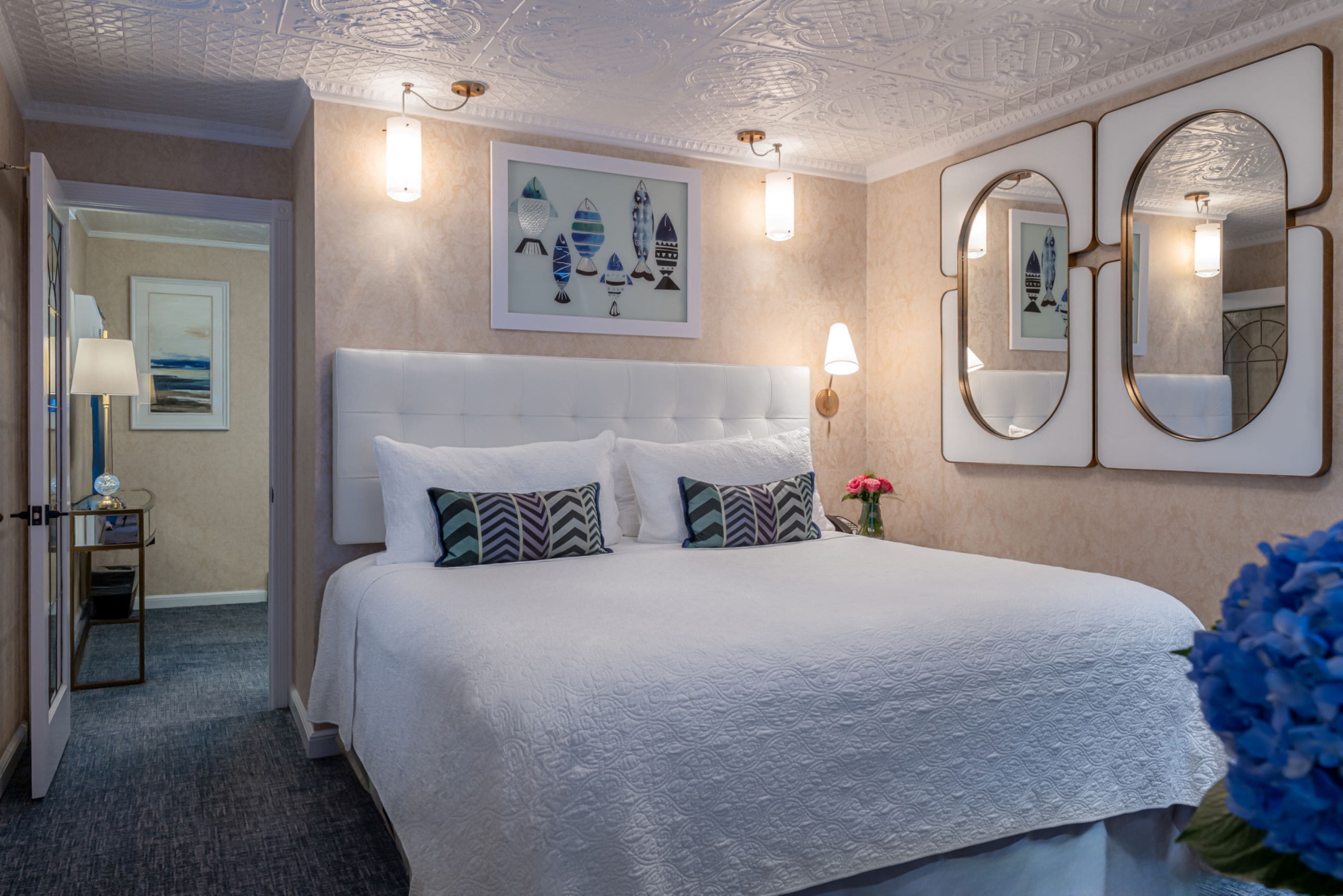 Hotellihuone, jossa on suuri sänky, yöpöytä lampun kanssa, seinällä oleva kehystetty taideteos ja peili.