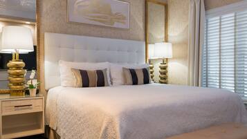 A hotel room with a large bed, two bedside tables with lamps, a headboard, and a window with blinds.