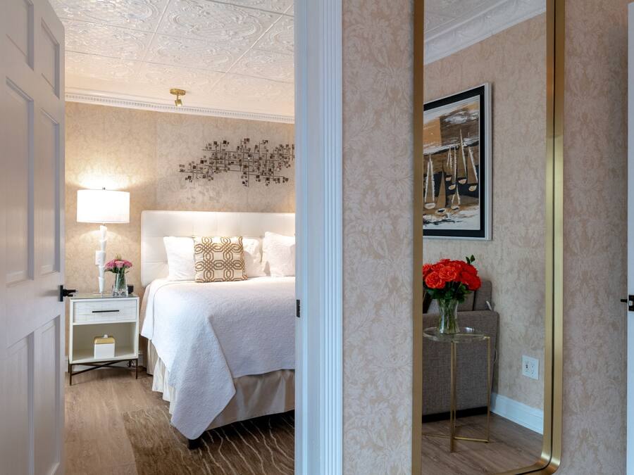 A hotel room with a large bed, a bedside table with a lamp, a vase with flowers, and a framed picture on the wall.