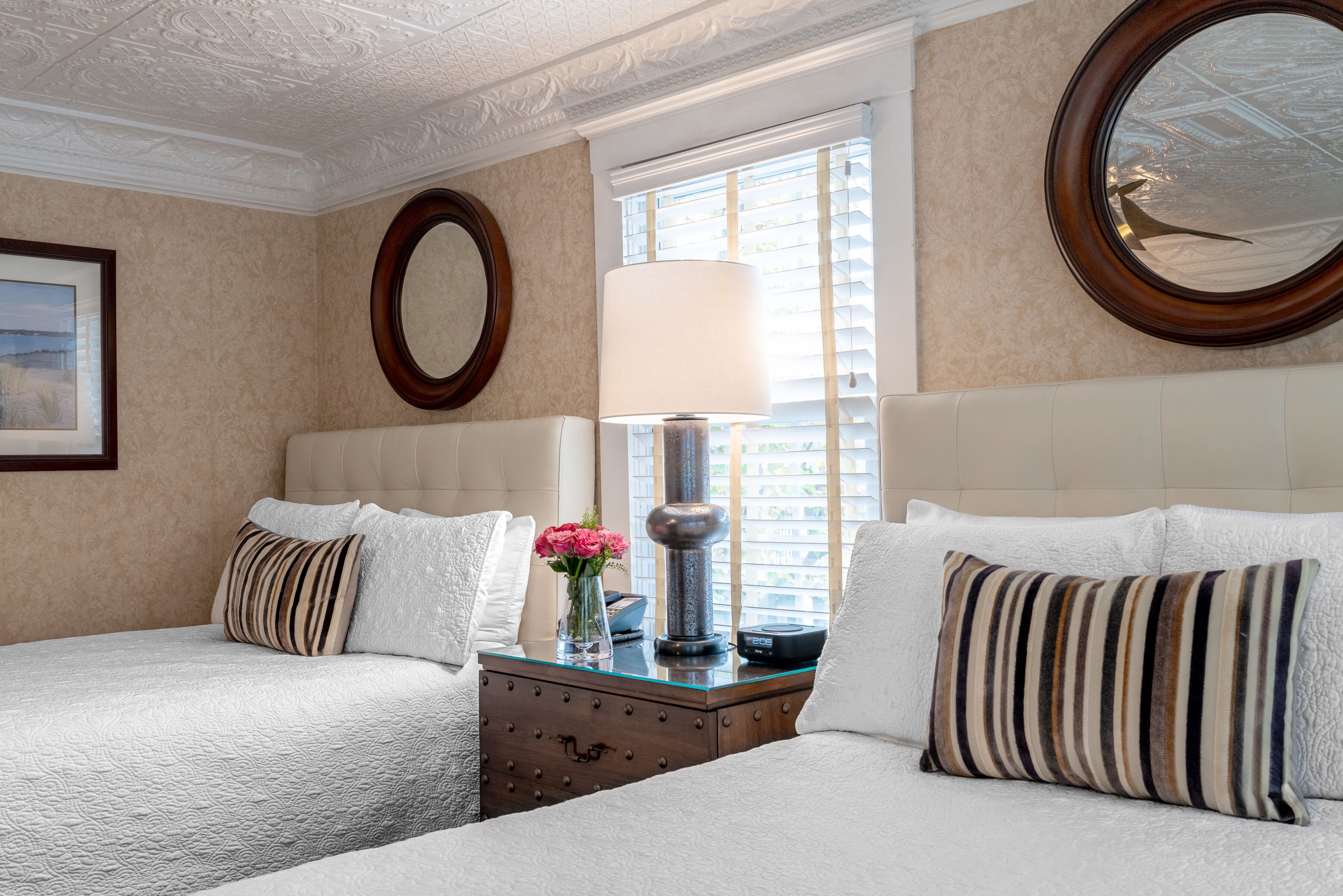 A hotel room with two beds, a dresser, a mirror, and a window with blinds.