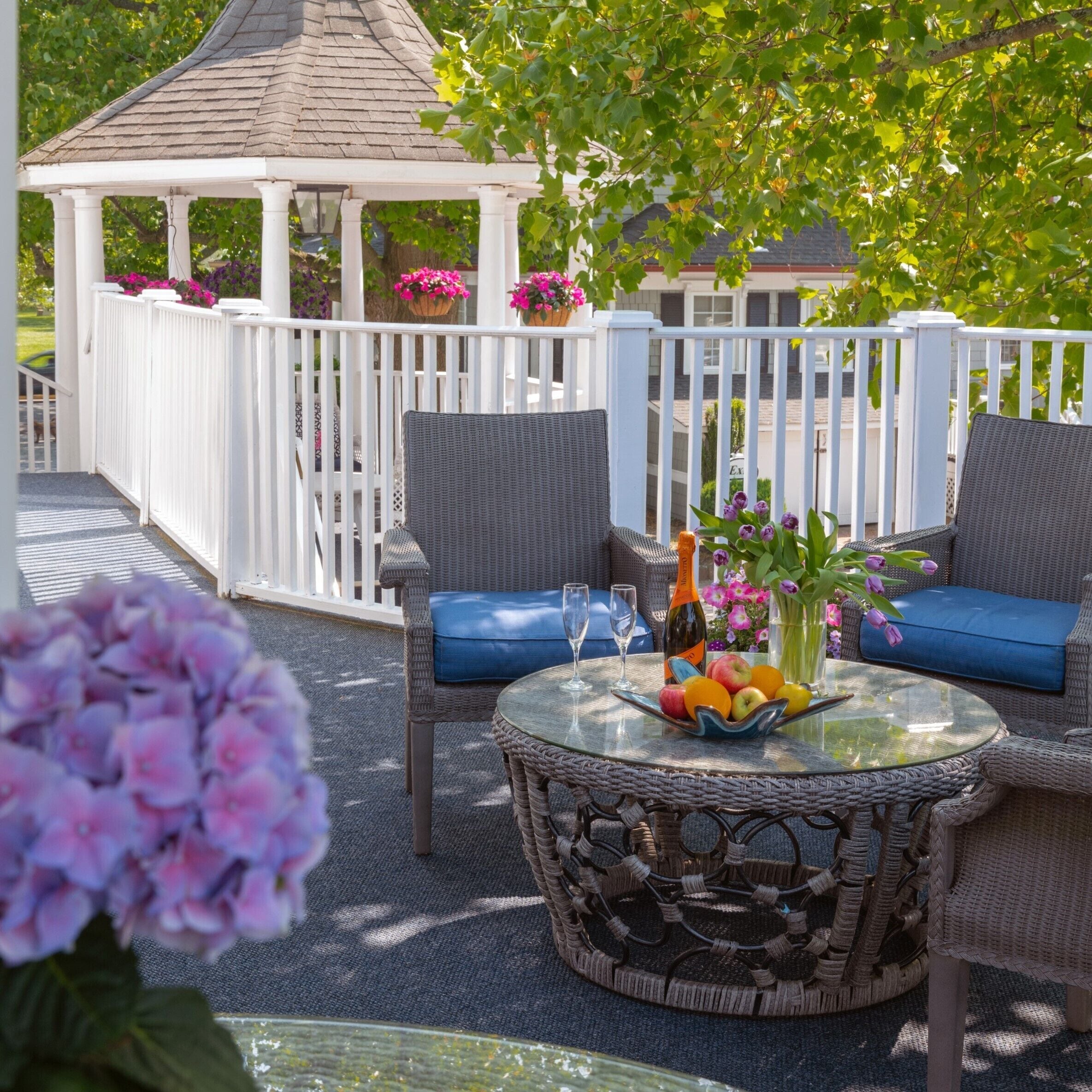 An outdoor patio with wicker furniture, a glass table, and a gazebo in the background.