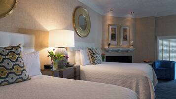 A hotel room with two beds, a nightstand, a lamp, a mirror, and a fireplace.
