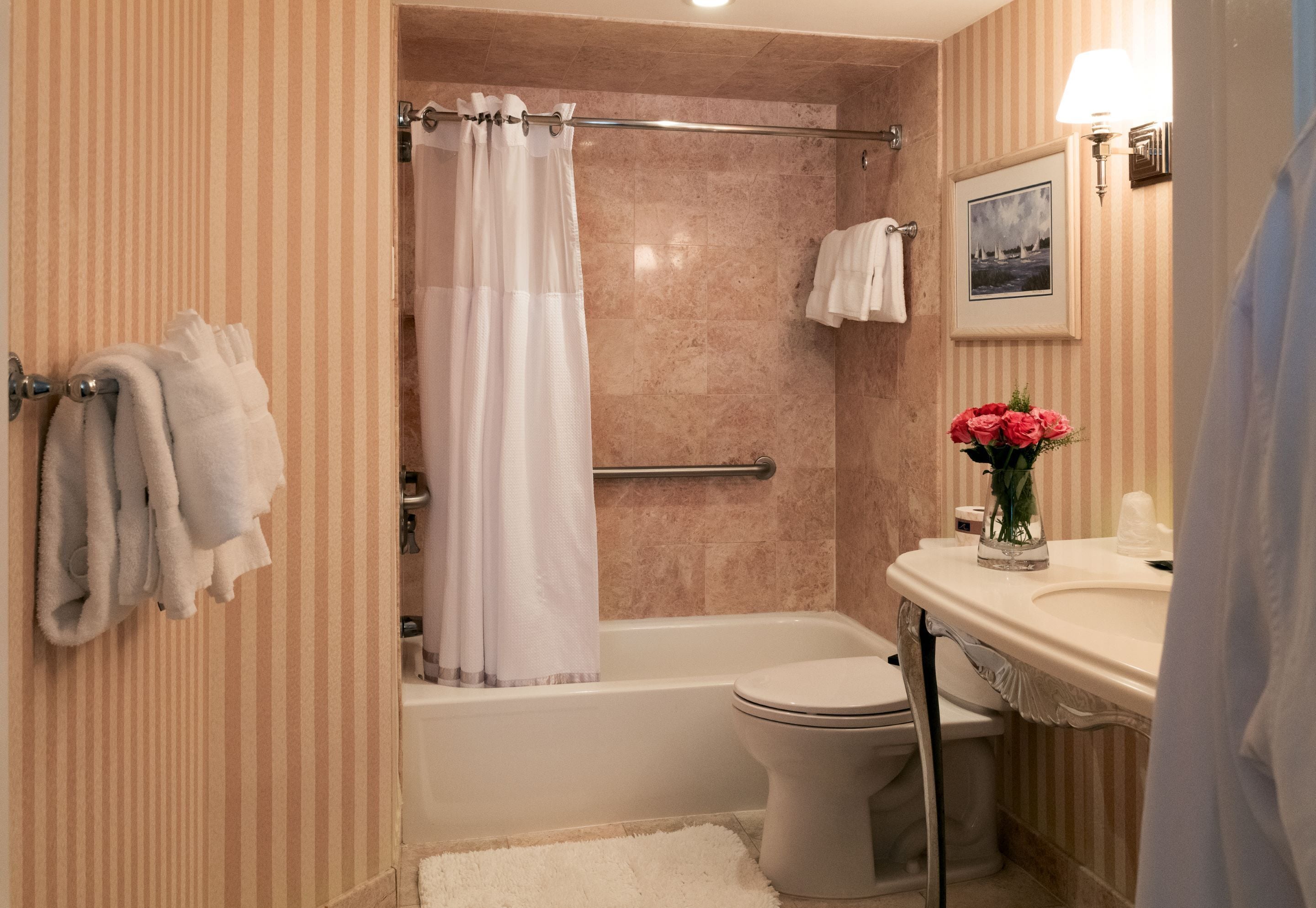 Un bagno con vasca, toilette e lavabo. Asciugamani appesi al muro e un quadro incorniciato sopra il lavabo.