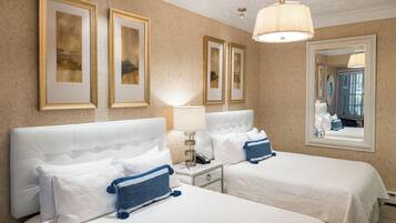 Quarto de hotel com duas camas, mesa de cabeceira, abajur e quadros na parede.