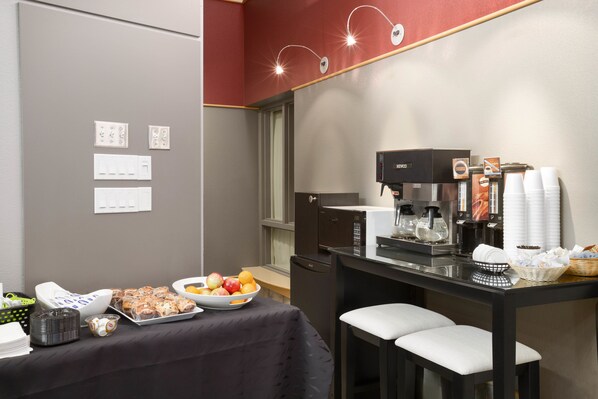 Une petite cuisine équipée d’une machine à café, de tasses et d’un panier de fruits.