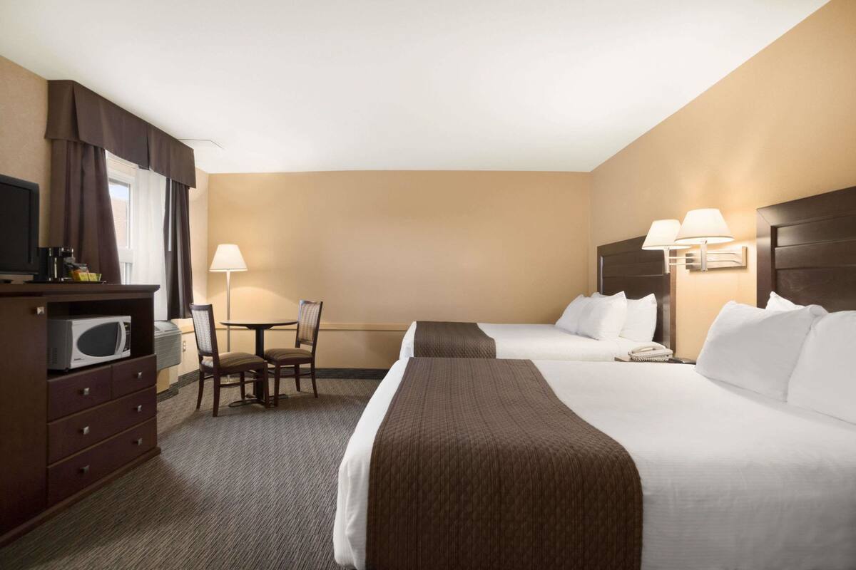 A hotel room with two beds, a desk, a chair, a microwave, a TV, and a lamp.
