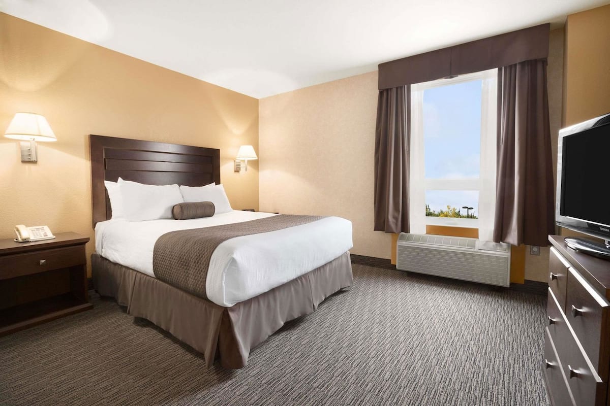 A hotel room with a bed, bedside lamps, a TV, a heater, and a window with curtains.