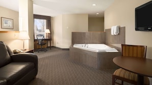 Hotelkamer met leren bank, bureau met stoel, ligbad, houten tafel met stoel en flatscreen televisie aan de muur.