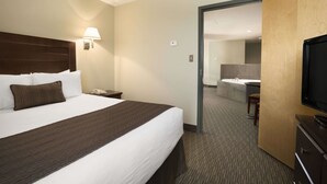Een hotelkamer met een groot bed, een bureau met een lamp, een televisie en een zichtbare badkamer door een geopende deur.