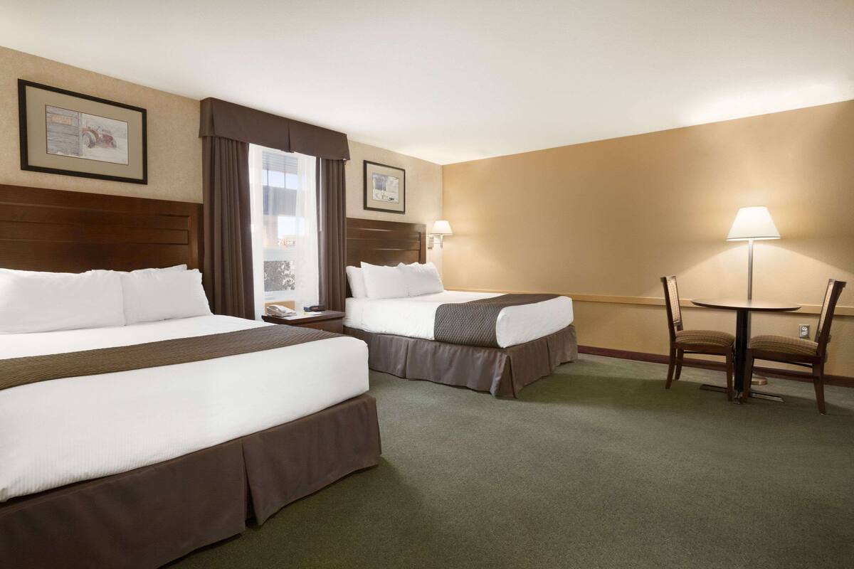 A hotel room with two beds, a desk, and a chair.