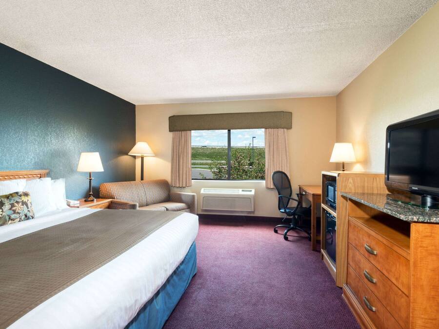 Una habitación de hotel con cama, dos lámparas de noche, un escritorio con computadora, televisión y ventana con cortinas.
