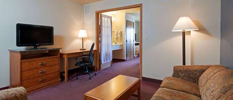 Een hotelkamer met televisie, bureau, kantoorstoel, bank en een lamp.