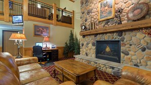 A spacious living area with leather sofas, a stone fireplace, and a television on the upper level. - AmericInn by Wyndham Rexburg BYUI (Rexburg)